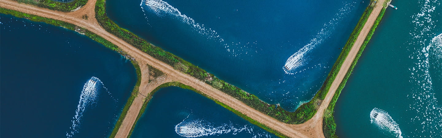 Aerial view of intersecting dirt road forming a cross over blue water bodies