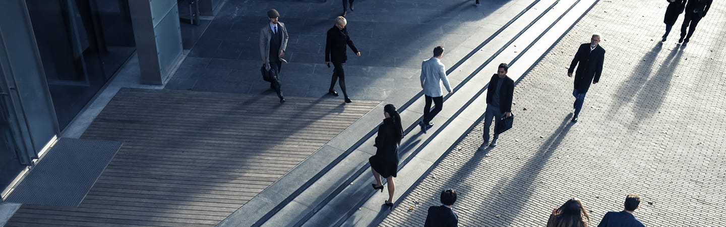 Aerial view of business professionals crossing a geometric walkway with dramatic shadows and lines.