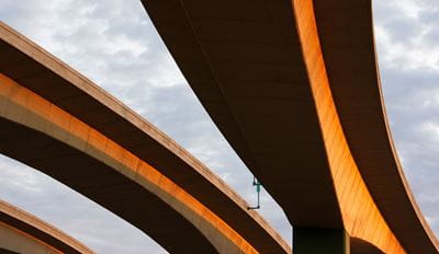 Concrete highway overpass structures photographed from below with golden sunlight against a cloudy sky.