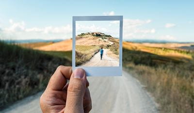A person holds a photo depicting a road leading to a house, showcasing a scenic residential view.