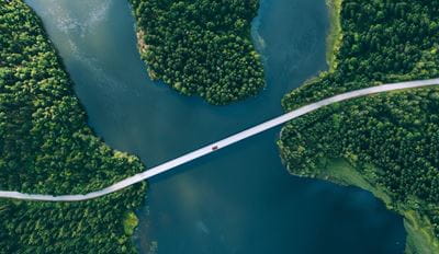 Aerial view of a narrow bridge over a tranquil river, surrounded by lush green forests.