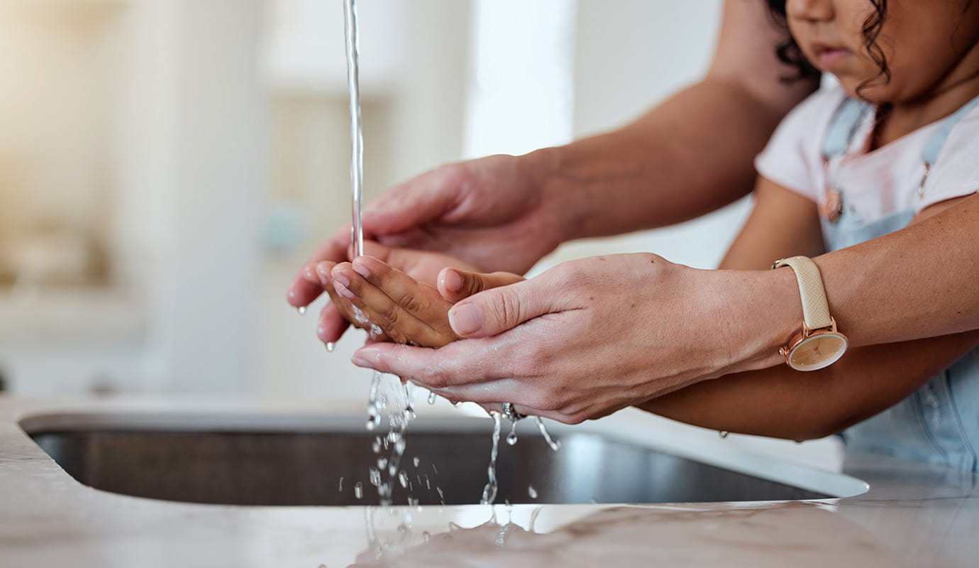 A young girl washes her hands under a faucet outside