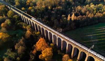 Train crossing a stone viaduct over autumn forest, aerial view