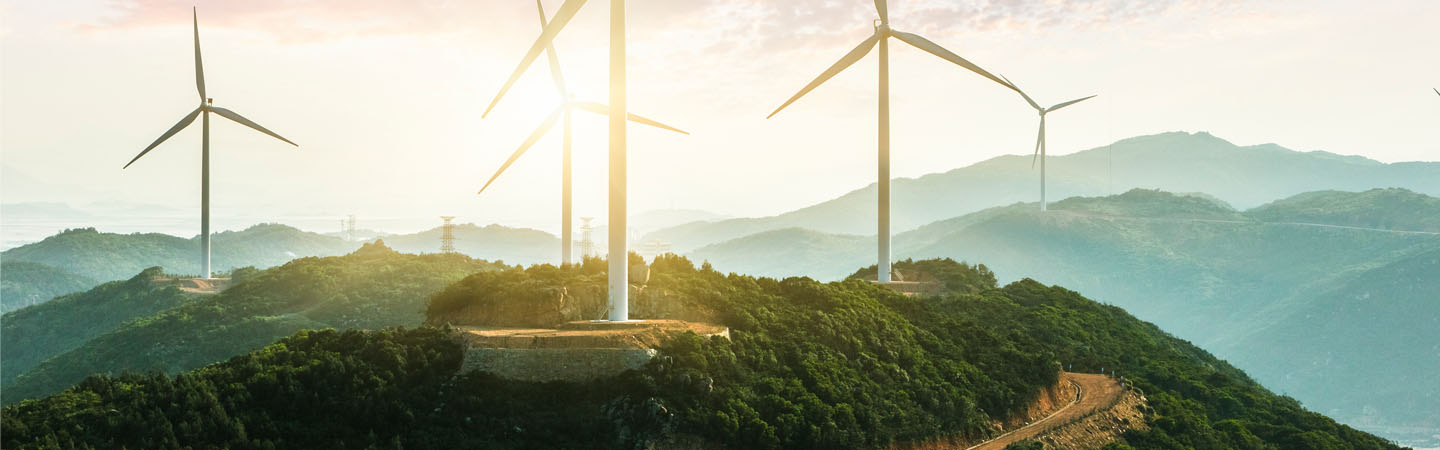 The sun rises behind a windmill farm on hills
