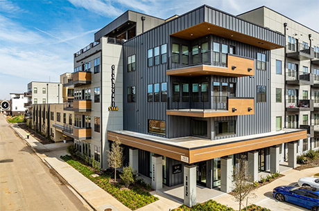 Apartment complex located at the corner of a street, featuring multiple floors and a modern architectural design.