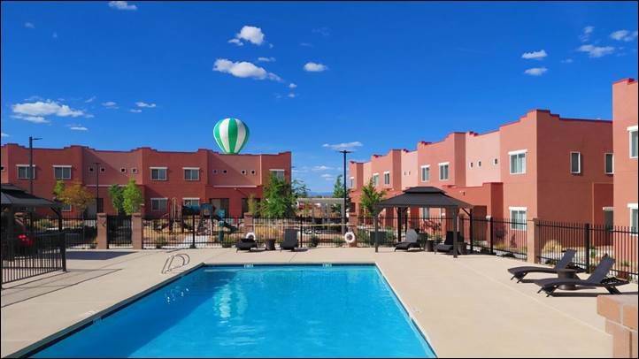 Sunny courtyard with a clear blue swimming pool, surrounded by pink stucco buildings. A hot air balloon floats above, adding a sense of tranquility.